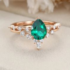 a ring with an emerald and white diamonds on the side, sitting on top of a cloth