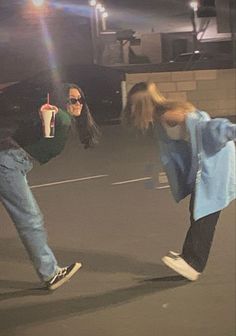 two people are dancing in the middle of an empty parking lot while one person holds up a drink