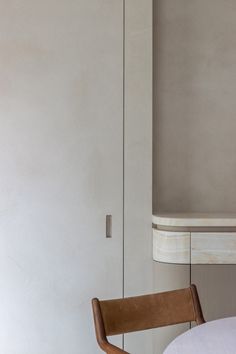 a white table and chair in front of a gray wall with a mirror on it