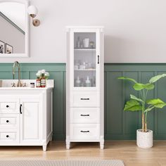 a bathroom with green walls and white cabinet next to a plant in a pot on the floor