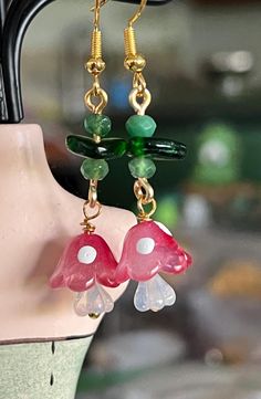 a pair of earrings is hanging from a mannequin's head with green and red beads