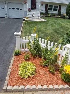 a white picket fence sitting in the middle of a flower bed next to a house