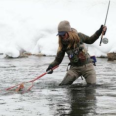 a woman standing in the water holding a fishing pole