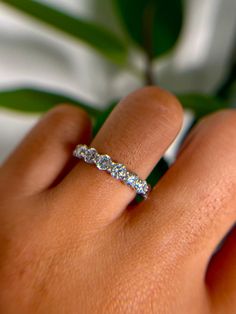 a woman's hand with a diamond ring on her left hand and a plant in the background