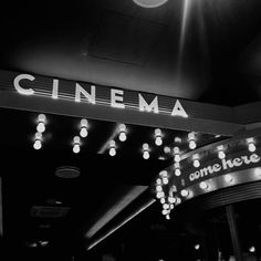 a black and white photo of a cinema sign with lights hanging from it's sides