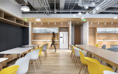 an office with yellow and white chairs, desks, and a man walking in the background