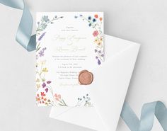 an envelope with a wax stamp on it next to a blue ribbon and some flowers