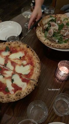 two pizzas sitting on top of a wooden table next to glasses and plates with silverware