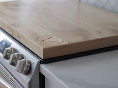 a wooden cutting board sitting on top of an oven with knobs and drawers next to it