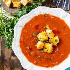 a white bowl filled with red sauce and croutons on top of a wooden table