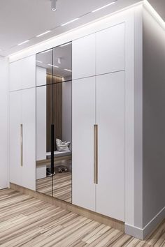 a white closet with mirrored doors and wooden flooring in an empty room, next to a bed