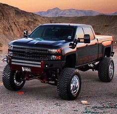 a large black truck parked on top of a dirt field next to a mountain range