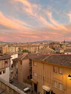 the sun is setting over an old city with tall buildings and cars parked on the street