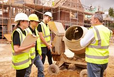 four men in yellow vests and hard hats are standing around a machine that is being worked on