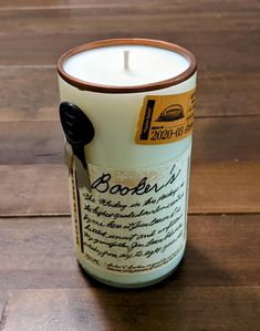 a candle that is sitting on a wooden floor next to a bottle with writing on it