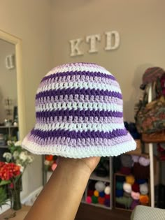 a hand holding up a purple and white crocheted hat