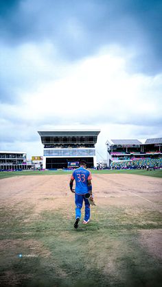 a baseball player standing on top of a field next to an empty ball field in front of a stadium