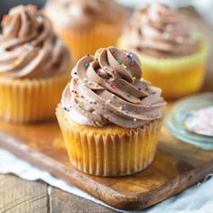 three cupcakes with chocolate frosting and sprinkles on a wooden tray