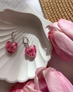 two pink heart shaped earrings sitting on top of a plate next to tulips