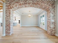 an empty living room with wood floors and brick archway leading into the dining room area