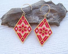 a pair of red and gold beaded earrings sitting on top of a piece of wood