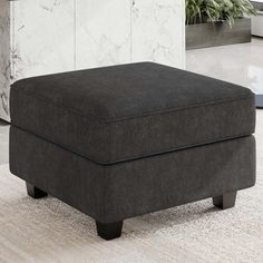 a large gray ottoman sitting on top of a white carpeted floor next to a potted plant