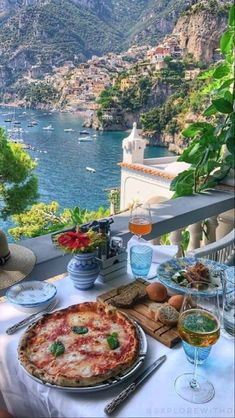 a table topped with pizza and drinks on top of a balcony next to the ocean