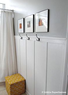 a white bathroom with three pictures hanging on the wall and a yellow stool in front of it