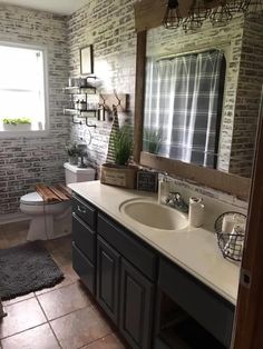 a bathroom with two sinks, a toilet and a brick wall in the shower area