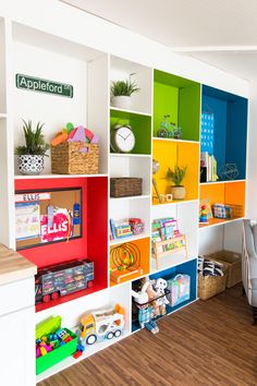 a room filled with lots of colorful bookshelves next to a white chair and desk