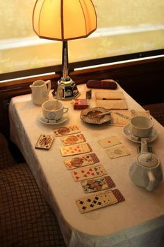 a table with cards and cups on it next to a lamp in front of a window