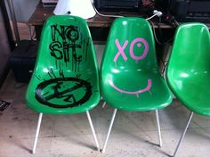 three green chairs with graffiti on them sitting in front of a computer keyboard and monitor