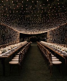 a long table set up for dinner with lights on the ceiling and chairs around it