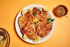 a white plate topped with chicken cutlets next to a bowl of mustard and seasoning