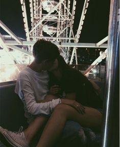 a man and woman sitting next to each other on a bench in front of a ferris wheel