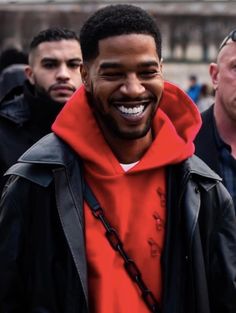 a man in a red hoodie smiles as he walks with other men behind him