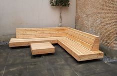 a wooden bench sitting in front of a brick wall next to a planter on the side of a building