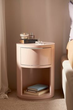 a nightstand with books on it next to a white couch in a room that has beige walls