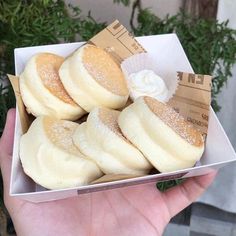 a person is holding a box full of sugared donuts with icing on them