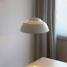 a table with a lamp hanging over it next to a window and curtained windows