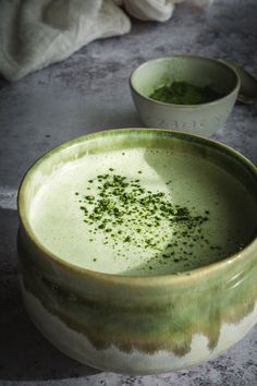 two bowls filled with green food sitting on top of a cement floor next to each other