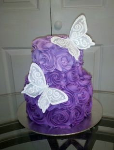 a purple cake with white butterflies on top and swirly icing, sitting on a table