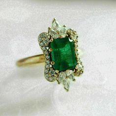 an emerald and diamond ring on a white surface