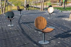 several wooden chairs sitting on top of a black floor next to trees and benches in a park