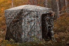 a man standing in the woods next to a camouflaged out shed with trees around it