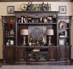 an ornate wooden entertainment center with lamps and pictures on the top shelf, in front of a beige wall