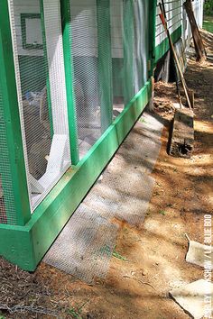 a chicken in a green coop on the side of a house with grass and dirt