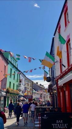 many people are walking down the street in front of colorful buildings and buntings