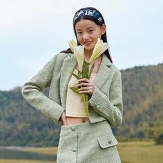 a young woman holding a flower in front of her face and wearing a green jacket