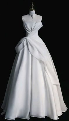 a white wedding dress with a large bow on the waist and neckline, in front of a black background